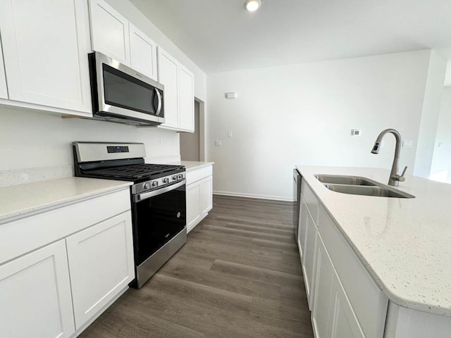 kitchen with appliances with stainless steel finishes, dark hardwood / wood-style floors, white cabinetry, sink, and light stone counters