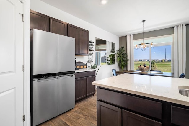 kitchen with decorative light fixtures, dark brown cabinets, stainless steel refrigerator, a notable chandelier, and light stone countertops