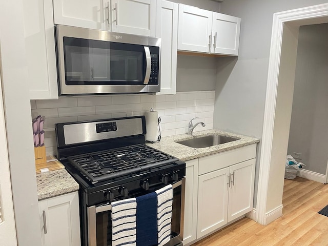 kitchen with sink, white cabinetry, light stone counters, light hardwood / wood-style flooring, and appliances with stainless steel finishes