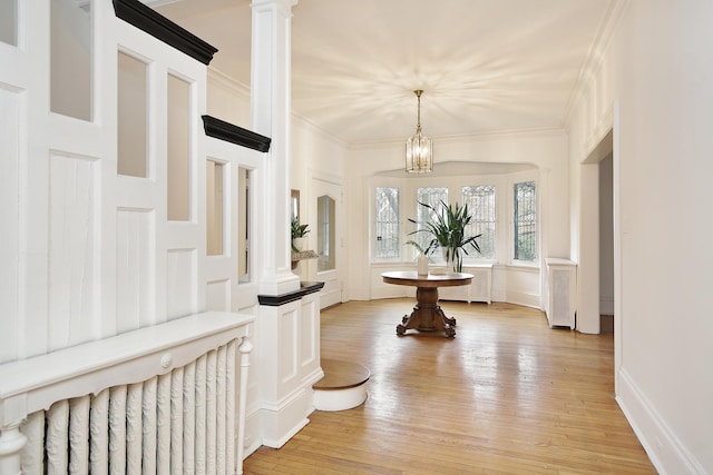 entryway with ornamental molding, a chandelier, decorative columns, and light wood-type flooring