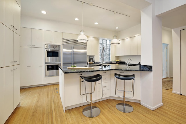 kitchen with dark stone countertops, a breakfast bar area, white cabinets, hanging light fixtures, and stainless steel appliances