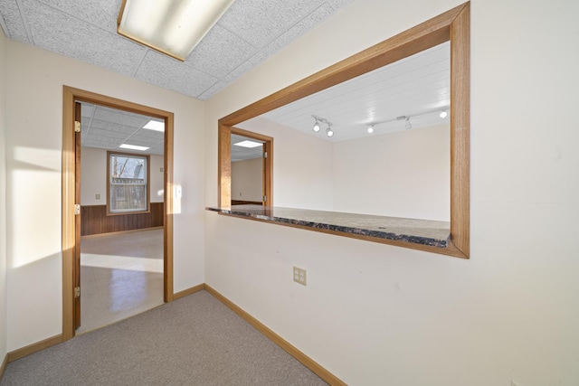 hallway featuring a paneled ceiling, rail lighting, carpet floors, and wood walls