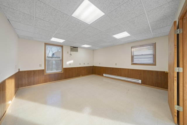 unfurnished room featuring a drop ceiling, a baseboard heating unit, and wood walls