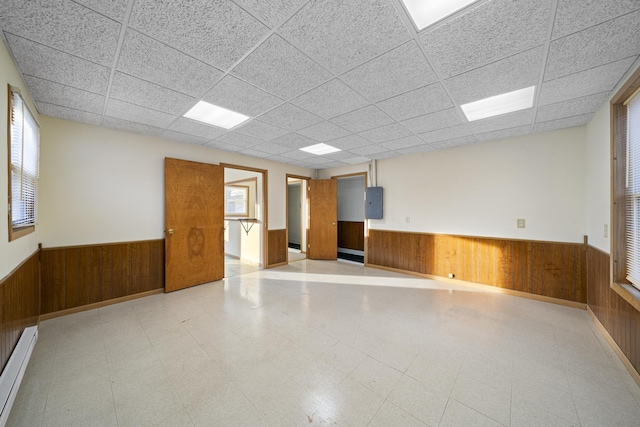 unfurnished room featuring a drop ceiling, a baseboard radiator, and wood walls