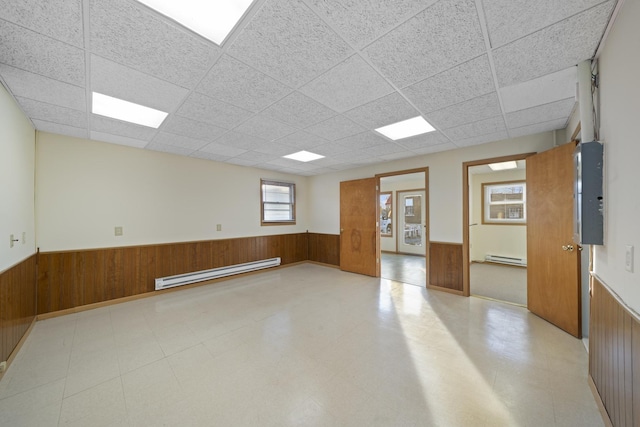 spare room with a paneled ceiling, baseboard heating, and wood walls