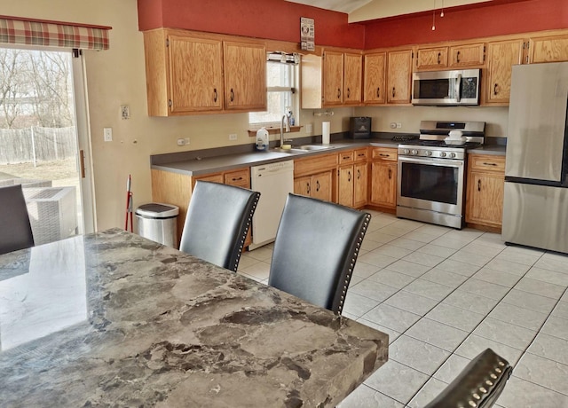 kitchen with light tile patterned flooring, a sink, stainless steel appliances, vaulted ceiling, and dark countertops