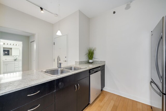 kitchen with sink, hanging light fixtures, stainless steel appliances, light hardwood / wood-style floors, and light stone countertops