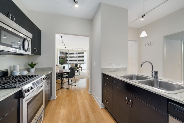 kitchen with rail lighting, sink, pendant lighting, stainless steel appliances, and light hardwood / wood-style floors