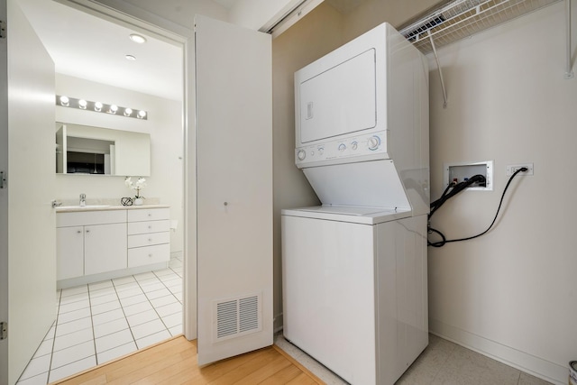 laundry area featuring stacked washer / drying machine, sink, and light wood-type flooring