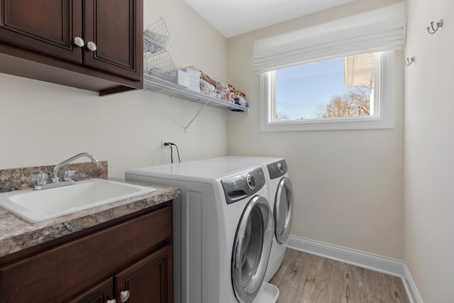 clothes washing area with cabinet space, baseboards, washer and clothes dryer, and a sink