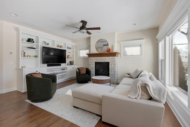 living room with dark wood-style floors, plenty of natural light, a stone fireplace, and baseboards