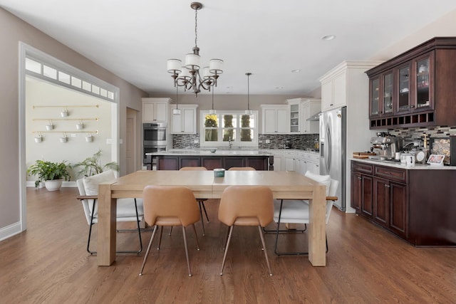 kitchen with pendant lighting, light countertops, glass insert cabinets, appliances with stainless steel finishes, and dark brown cabinets