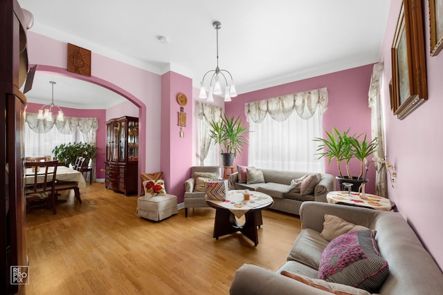 living room with crown molding, a healthy amount of sunlight, an inviting chandelier, and light hardwood / wood-style floors