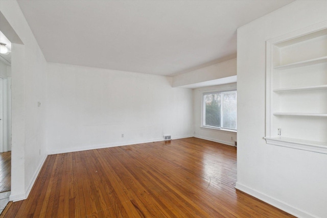 spare room with built in shelves and hardwood / wood-style flooring