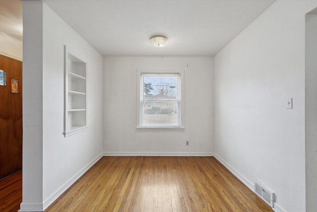 empty room with light hardwood / wood-style flooring and built in shelves