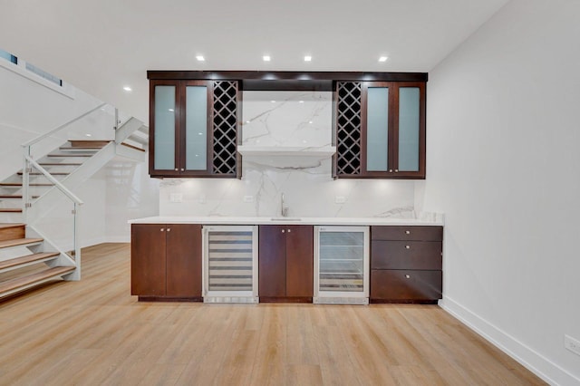 bar with wine cooler, decorative backsplash, dark brown cabinets, and light wood-type flooring