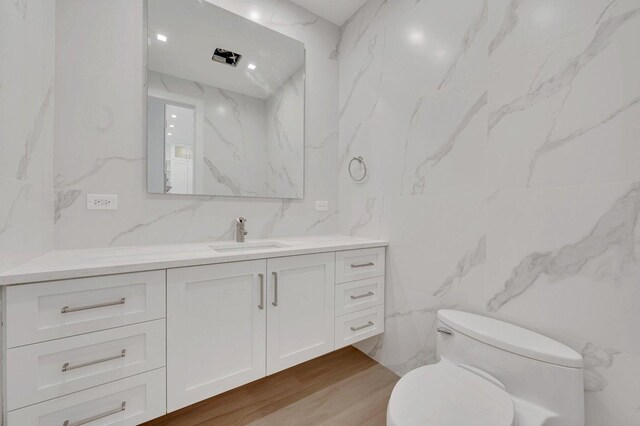 bathroom with vanity, toilet, hardwood / wood-style floors, and tile walls