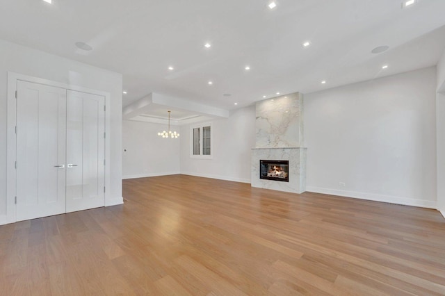 unfurnished living room featuring a high end fireplace, a chandelier, and light wood-type flooring