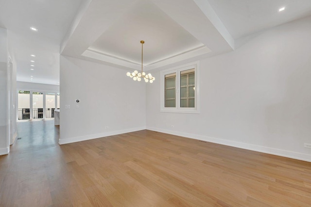 empty room with light hardwood / wood-style flooring, an inviting chandelier, and a tray ceiling