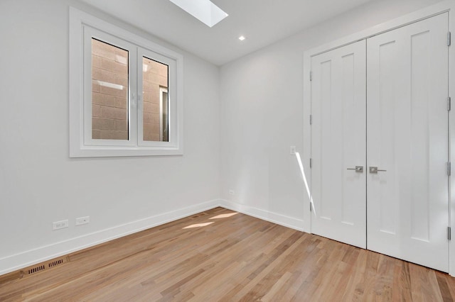 spare room featuring a skylight and light hardwood / wood-style flooring