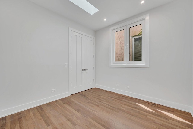 unfurnished room with a skylight and light hardwood / wood-style floors