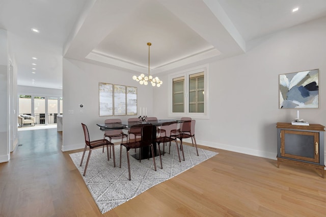 dining area featuring a notable chandelier, a tray ceiling, and light wood-type flooring