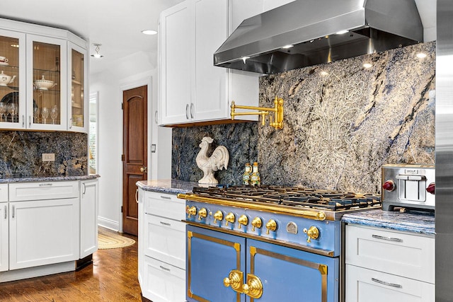 kitchen with white cabinets, dark stone counters, wall chimney exhaust hood, and range