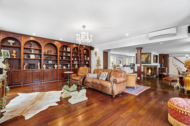 living room featuring dark wood-type flooring, a wall unit AC, decorative columns, a notable chandelier, and a fireplace