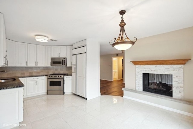 kitchen with a sink, white cabinetry, stainless steel appliances, decorative backsplash, and a multi sided fireplace