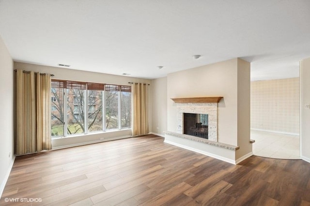 unfurnished living room with hardwood / wood-style flooring and a stone fireplace