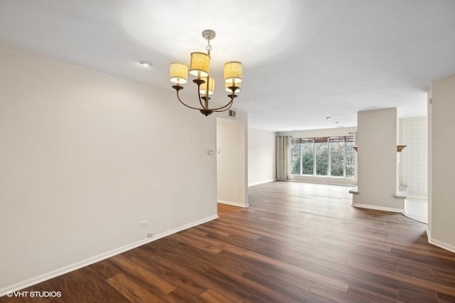 empty room with dark wood-type flooring and a notable chandelier