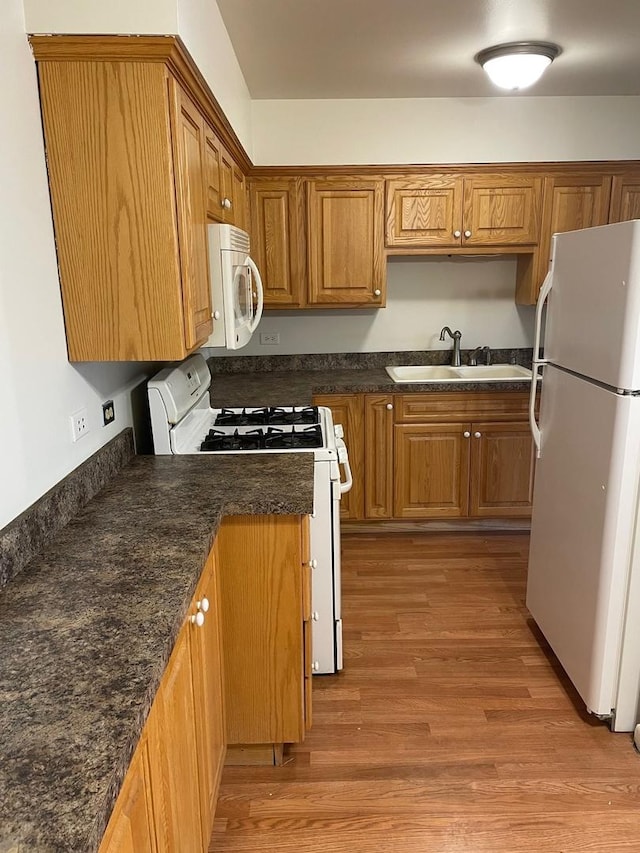 kitchen featuring sink, dark stone counters, white appliances, and light wood-type flooring