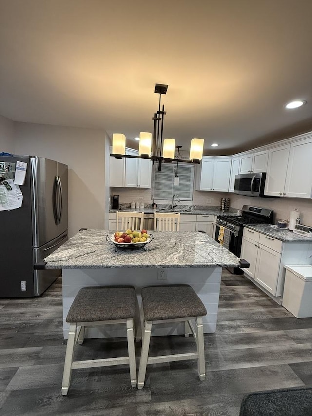 kitchen with hanging light fixtures, stainless steel appliances, a center island, light stone countertops, and white cabinets