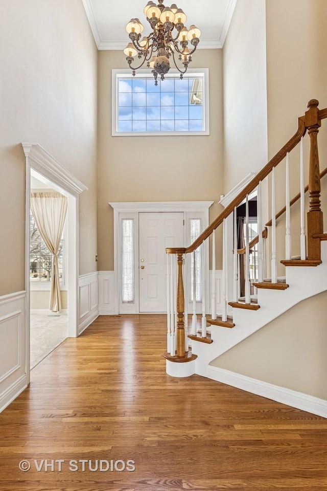 foyer with wainscoting, crown molding, an inviting chandelier, and wood finished floors