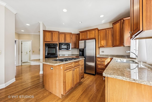 kitchen with light wood finished floors, appliances with stainless steel finishes, a sink, and light stone counters