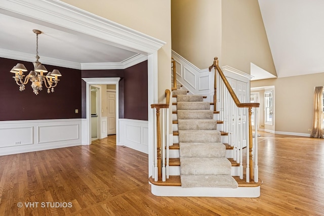 staircase featuring crown molding, a wainscoted wall, a notable chandelier, and wood finished floors