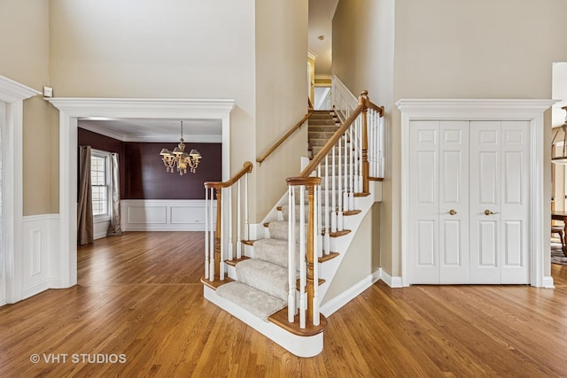 staircase featuring a chandelier, a wainscoted wall, a high ceiling, and wood finished floors