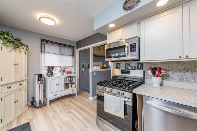 kitchen featuring appliances with stainless steel finishes, white cabinets, light wood-type flooring, and decorative backsplash