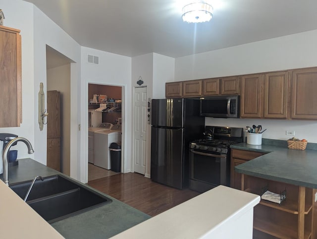 kitchen with dark hardwood / wood-style floors, appliances with stainless steel finishes, sink, and washing machine and dryer