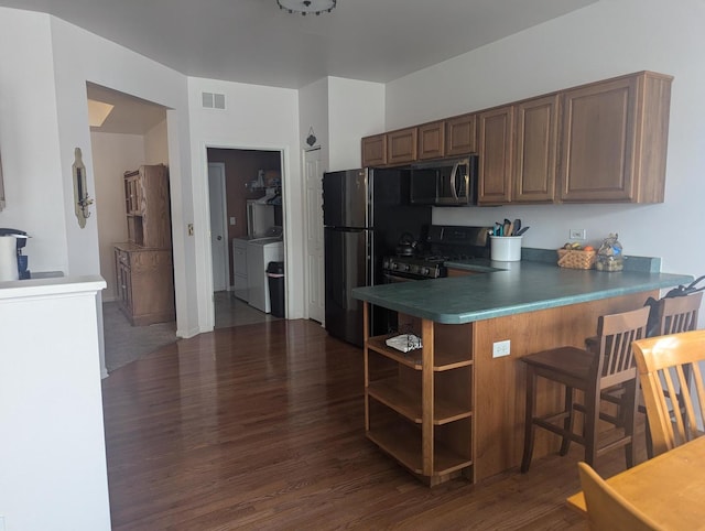 kitchen featuring dark hardwood / wood-style flooring, black refrigerator, gas range oven, separate washer and dryer, and kitchen peninsula