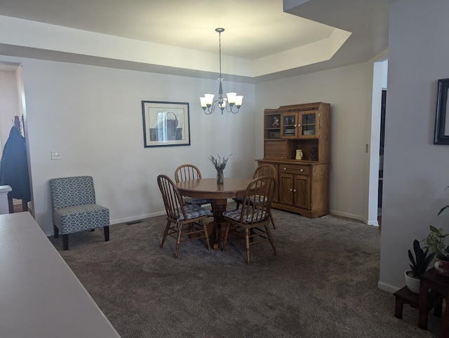 dining area featuring a notable chandelier, dark carpet, and a raised ceiling