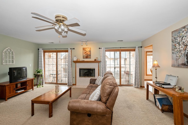 living room featuring ceiling fan, light colored carpet, a healthy amount of sunlight, and a tiled fireplace