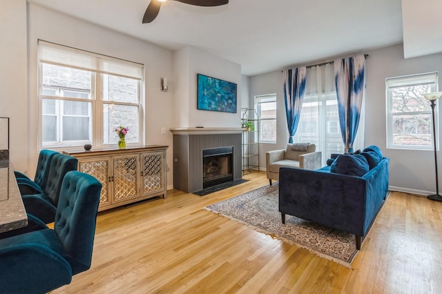 living room featuring a fireplace with flush hearth, wood finished floors, a ceiling fan, and baseboards