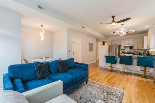 living area with a ceiling fan, visible vents, light wood-style flooring, and baseboards