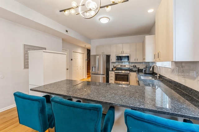 kitchen with appliances with stainless steel finishes, dark stone countertops, a peninsula, a sink, and backsplash