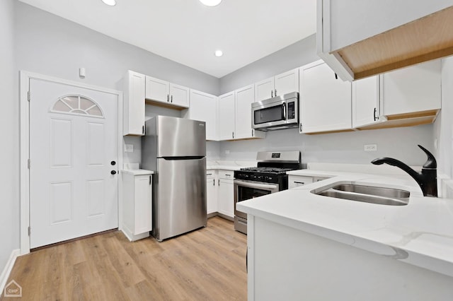 kitchen featuring sink, white cabinetry, stainless steel appliances, light stone countertops, and light hardwood / wood-style floors