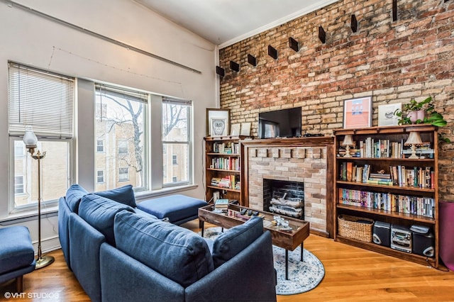 living room featuring a brick fireplace, brick wall, baseboard heating, and wood finished floors