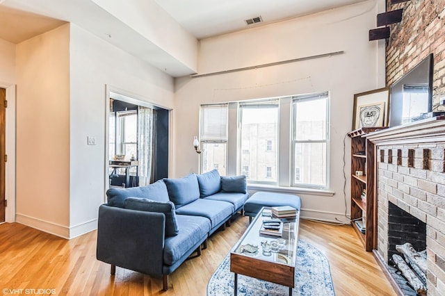 living room with light wood-type flooring, a brick fireplace, baseboards, and visible vents