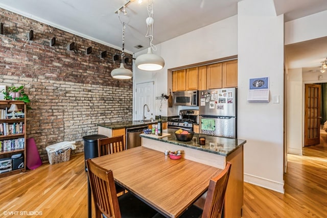 dining space with light wood-type flooring, rail lighting, brick wall, and baseboards