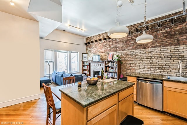 kitchen with brick wall, a fireplace, a sink, stainless steel dishwasher, and light wood finished floors